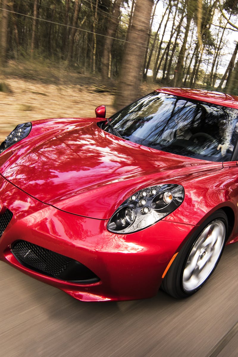 A sleek red sports car driving fast on a forest road, showcasing speed and luxury.