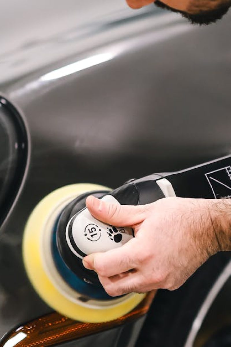 A man meticulously polishing a luxury sports car in a garage, focusing on the front section.