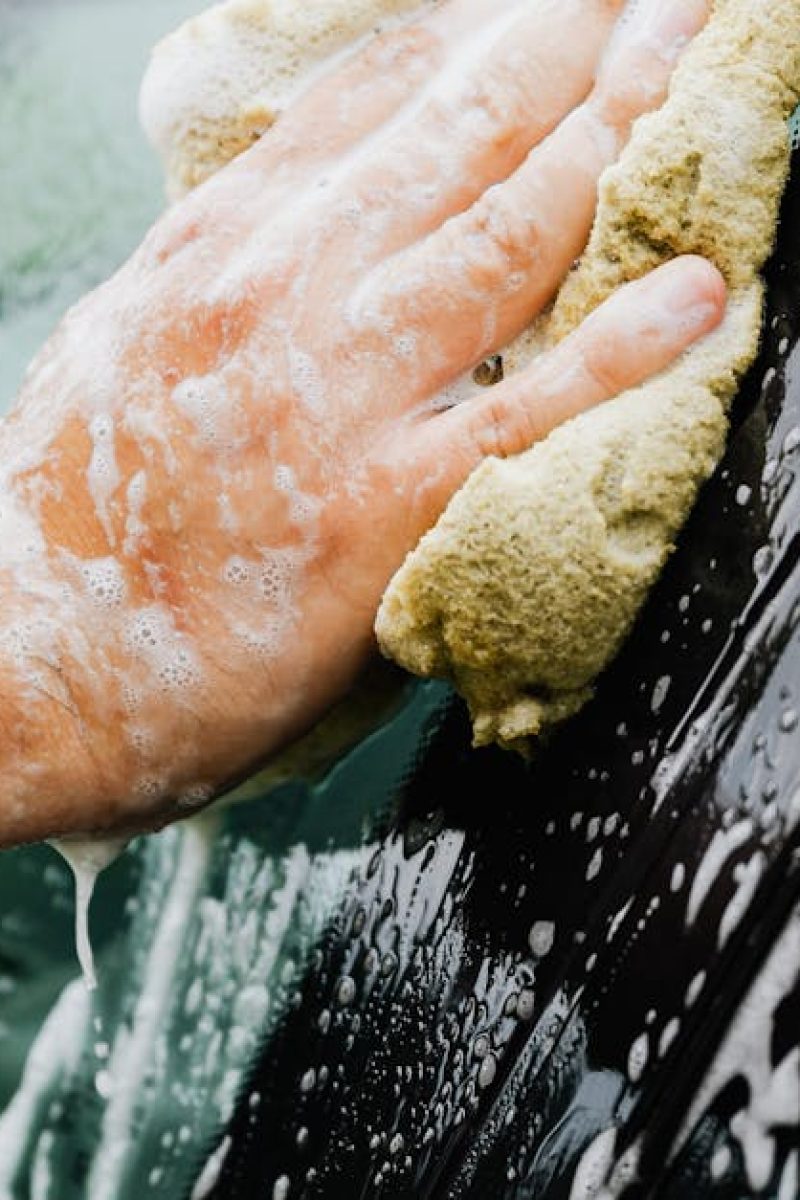Close-up of a person washing a car window with a sponge and soap suds outside.
